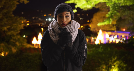 Wall Mural - Attractive young black woman wearing cozy hat and scarf on cold night outside