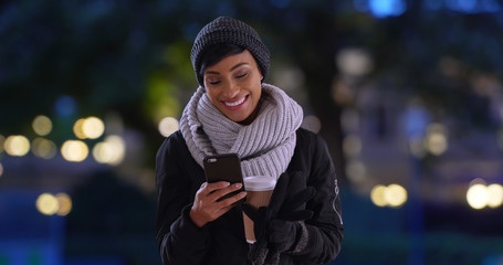 Beautiful young black woman with coffee reads text message on her phone