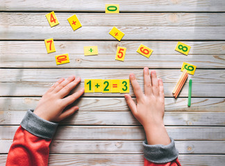 First-grader learn to count. The child decides a mathematical example. 1 + 2 = 3. Basic knowledge.