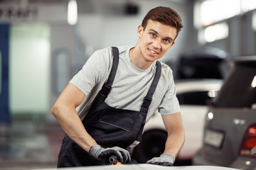 Wall Mural - A young man is smiling while polishing a car at a vehicle maintenance