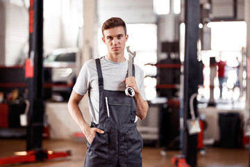 Wall Mural - A good-looking automechanic is standing at a car repair service 