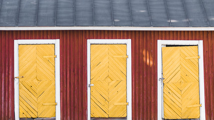 Wall Mural - Three vintage yellow doors in a red wooden house with blue roof. Scandinavian design.