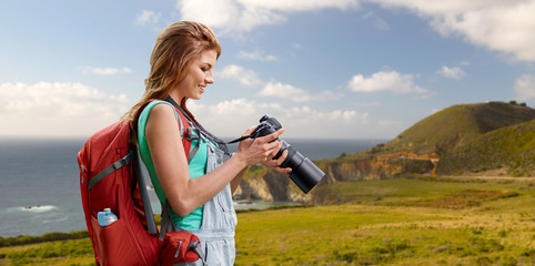 Wall Mural - travel, tourism and photography concept - happy young woman with backpack and camera photographing over big sur coast of california background