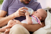 Family, Parenthood And People Concept - Close Up Of Father Feeding Little Daughter With Baby Formula From Bottle At Home