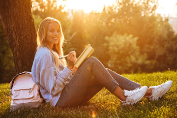 Wall Mural - Portrait of a happy young girl sitting on a grass