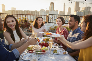 Friends Gathered On Rooftop Terrace For Meal With City Skyline In Background