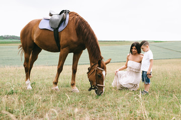 mother and son looking at brown horse on green field