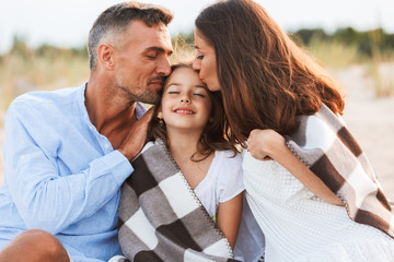 Parents hugging outdoors at the beach with their daughter.