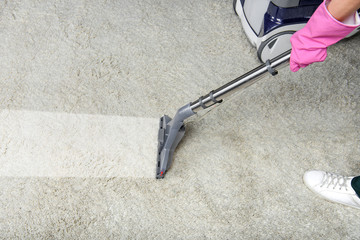 Cropped shot of person cleaning white carpet with vacuum cleaner