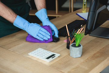 Cropped shot of professional cleaner in rubber gloves cleaning computer mouse on office table