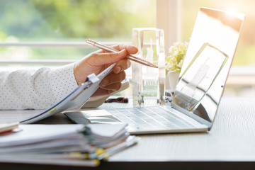 Wall Mural - Businessman hands holding pen for working in Stacks of paper files searching information business report papers and piles of unfinished documents achieves on laptop computer desk in modern office