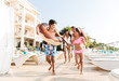 © Drobot Dean - Portrait of smiling kids and parents walking near swimming pool, and carrying rubber ring outside hotel during vacation