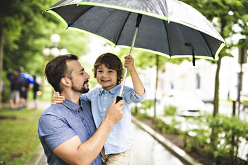 Father and child on a rainy day in a park with umbrella