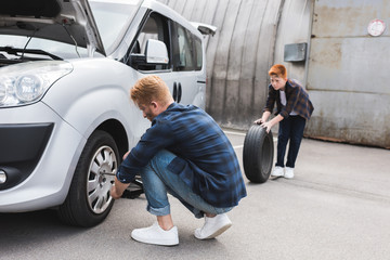 father changing tire in car with wheel wrench, son holding tire