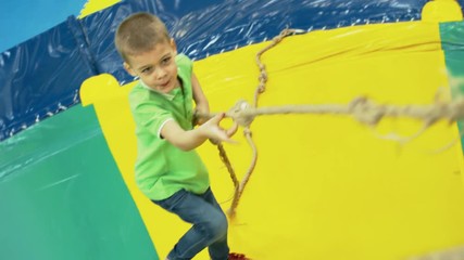 Wall Mural - Front view of playful little boy climbing inflatable structure in children play center using climbing rope