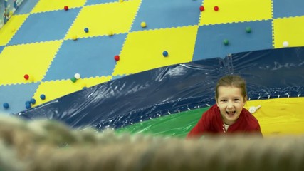 Wall Mural - Front view of cute smiling girl of primary school age climbing inflatable mountain in children play center