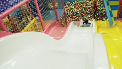 Wall Mural - Rear view of playful little boy having fun on plastic slides in children play center and sliding down into ball pool