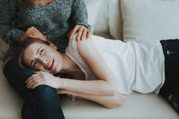 Upset Young Girl Lying on Mother's Legs on Sofa.