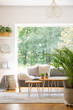 Plant and wooden tables in bright living room interior with grey sofa and window. Real photo