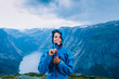 © Iryna - Happy woman zip up blue sportive jacket before rain, relaxing and smiling in cliff during trip Norway. Trolltunga hiking route