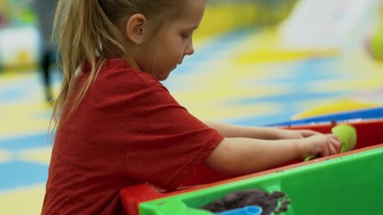 Wall Mural - Side view of adorable little girl playing in sandbox in indoor amusement park and forming shapes of sand with spade and molds