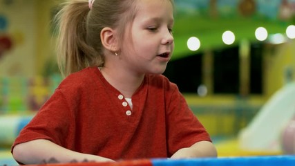 Wall Mural - Medium shot of interested little girl counting sand molds with finger when playing with friends in sandbox of indoor amusement park