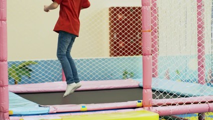 Wall Mural - Medium shot of little girl of primary school age jumping and bouncing on indoor trampoline in children play center