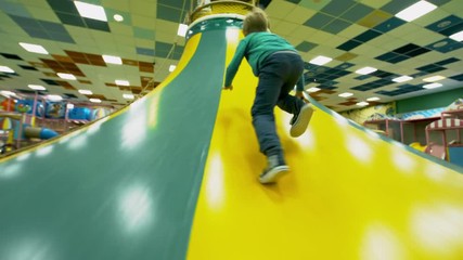 Wall Mural - Follow shot of active little boy running towards inflatable mountain and trying to climb it in children play center, rear view