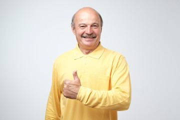 Wall Mural - Handsome, bald man with his thumb up in sign of optimism on white background