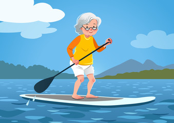 Senior woman on a stand up paddle board. Cute grandma wearing rash guard and shorts paddling on calm water, trees and mountains in the background. Healthy active lifestyle, water sports for seniors.