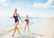 © Alliance - happy young mother and daughter in swimsuit on beach running