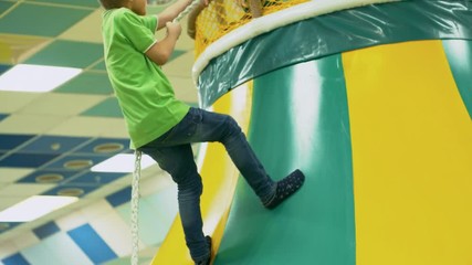 Wall Mural - Rear view of young boy of primary school age climbing inflatable structure using climbing rope when spending time with friend in playroom