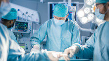 Diverse Team Of Professional Surgeon, Assistants And Nurses Performing Invasive Surgery On A Patient In The Hospital Operating Room. Surgeon Use Instruments. Real Modern Hospital