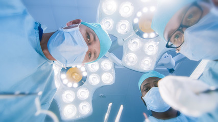 Wall Mural - Low Angle Shot POV Patient View: Two Professional Surgeons Holding Surgical Instruments Starting Surgery.