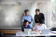 © Prathankarnpap - Group of young businessman working and communicating while sitting at the office desk together with colleagues sitting in the background,Startup business.