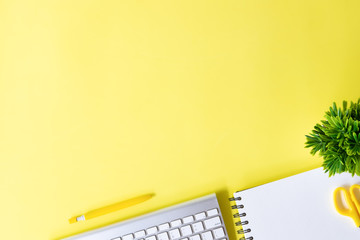 Above Office desk with computer keyboard, notebook paper, pen and plant decoration on yellow background top view mock up.