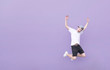 © bodnarphoto - Young man in a white T-shirt and black shorts in a jump on a purple background. Emotional teen jumps against the background of a purple wall