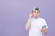 © bodnarphoto - Surprised young man standing against a background of pastel purple walls, looking at smartphone and listening to music on headphones. Emotional student on a purple background