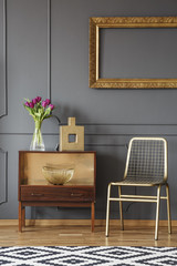 Wall Mural - Gold chair next to wooden cabinet with flowers in grey interior with mockup. Real photo