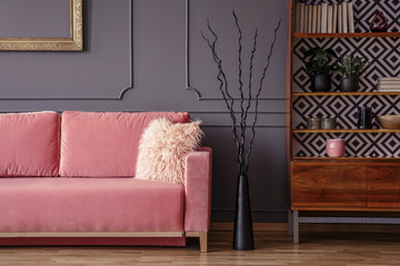 Wall Mural - Pink sofa next to black decor and wooden cabinet in vintage living room interior. Real photo