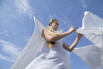 Girl teenager is hung up white sheets on clothesline fixing them with clothespins