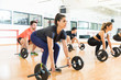 Woman Picking Up Barbell While Exercising With Friends In Gym