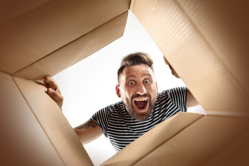 The surprised man unpacking, opening carton box and looking inside. The package, delivery, surprise, gift lifestyle concept. Human emotions and facial expressions concepts