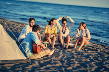 summer, vacation, holiday, happy people concept- Happy friends together relaxing with playing guitar and sing a song on sea beach.