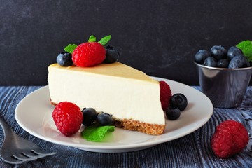 Poster - Slice of cheesecake with blueberries and raspberries on a plate, close up scene with a dark background