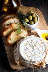 Wall Mural - Baked camembert cheese. Fresh Brie cheese and a slice on a wooden board with nuts, honey, rosemary, baguette bread grilled toasts and leaves. Brie type of cheese. Italian, French cheese.