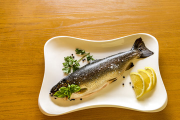 Raw fish rainbow trout with lemon and greens on white dish