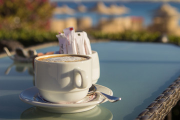 Wall Mural - white cup of coffee on the table at sea. Summer holiday concept.