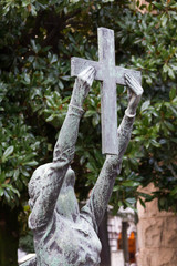 Milano, Italy. 2018/2/8. A statue of a woman holding up a cross on a tombstone at the Cimitero Monumentale (