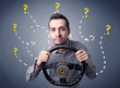 © ra2 studio - Young man holding black steering wheel with question marks around him